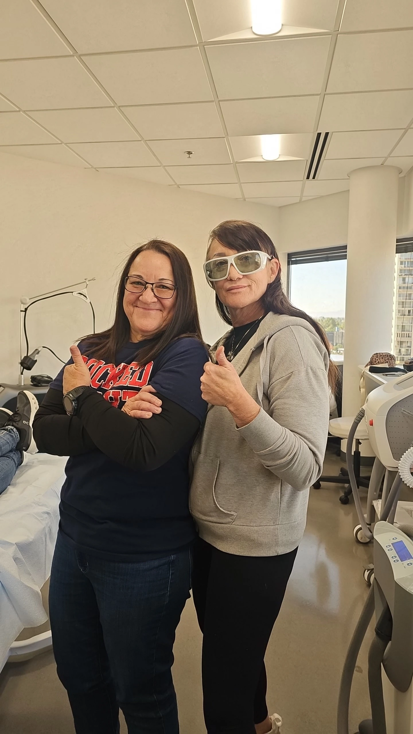 Two women smiling and giving thumbs up in a clinic.