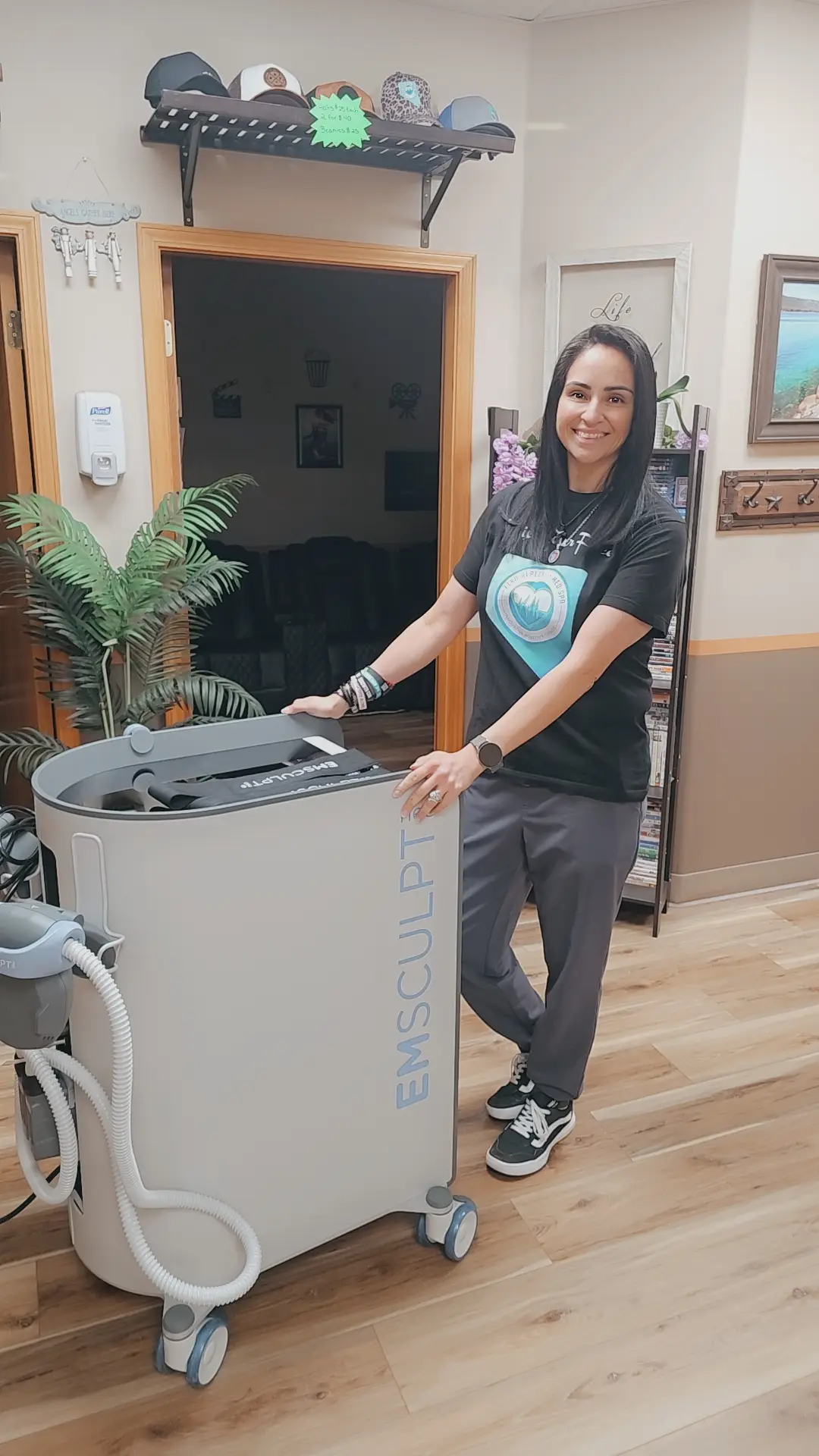 Woman smiling with EMSculpt device in a spa or clinic setting.