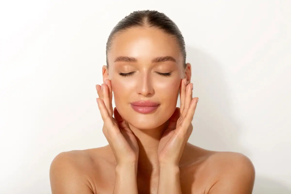 Woman with glowing skin touching face at Elko Replenish Med Spa