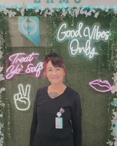 Licensed massage therapist at Elko Refresh Med Spa in Elko, Nevada, standing in front of wellness-themed neon signage.