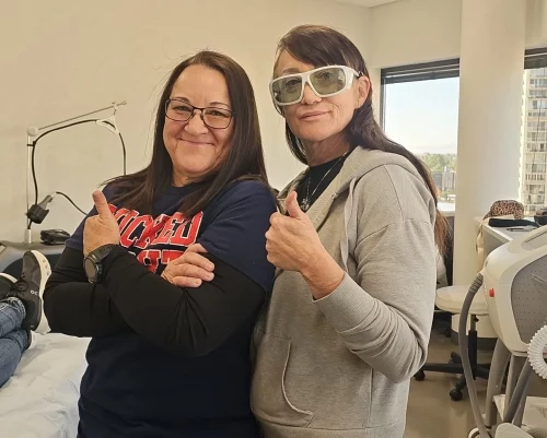 Two women smiling and giving thumbs up in a clinic.