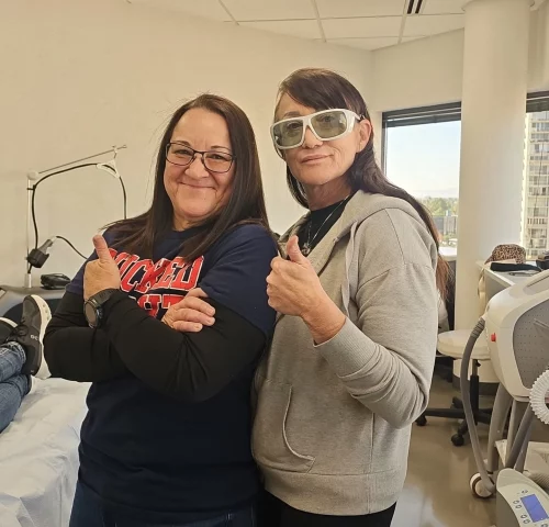 Two women smiling and giving thumbs up in a clinic.